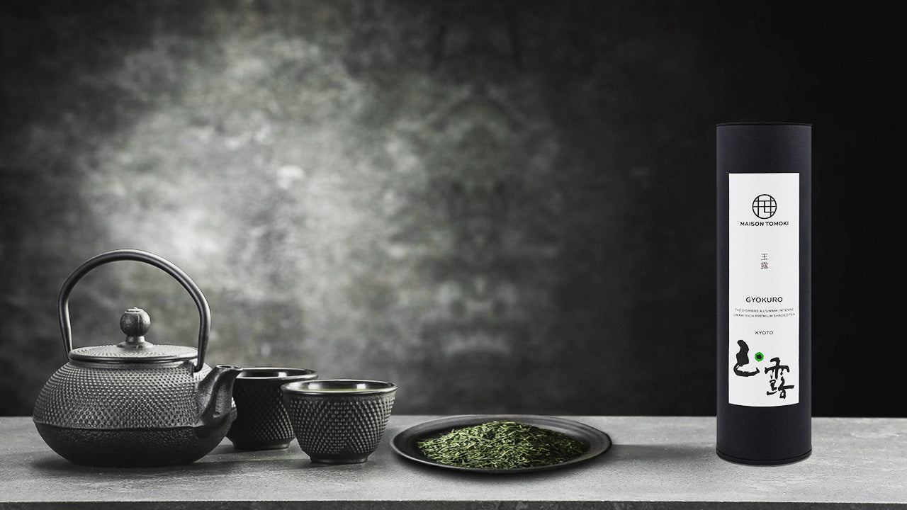 Deep green gyokuro tea leaves displayed alongside a black Kyusu teapot and yunomi teacups, featuring a Maison Tomoki tin can of premium Kyoto Uji gyokuro - Maison Tomoki